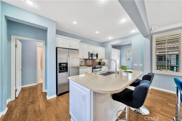 kitchen featuring light wood finished floors, a sink, stainless steel appliances, a kitchen bar, and backsplash