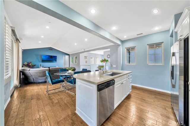 kitchen with a sink, lofted ceiling, stainless steel appliances, white cabinetry, and wood-type flooring