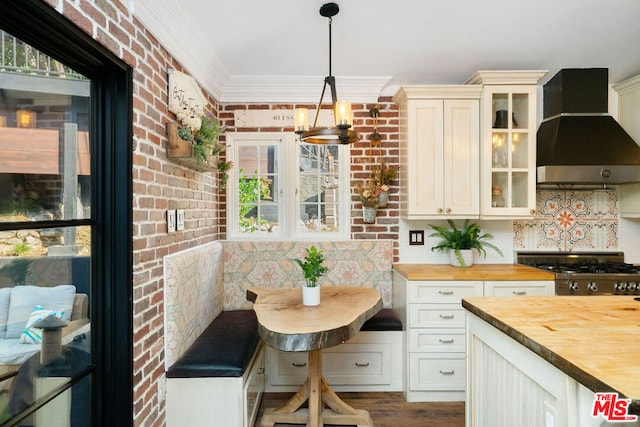 kitchen with range, butcher block counters, hanging light fixtures, breakfast area, and wall chimney exhaust hood