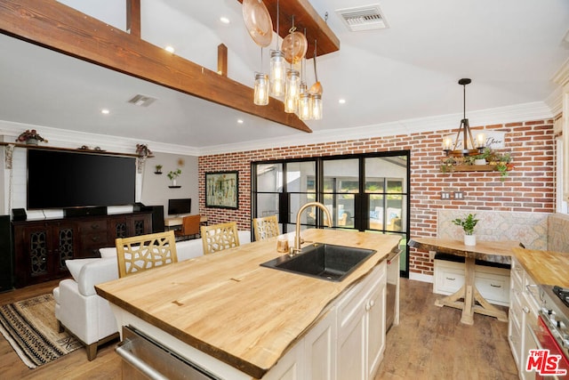 kitchen with sink, a kitchen island with sink, pendant lighting, and wooden counters