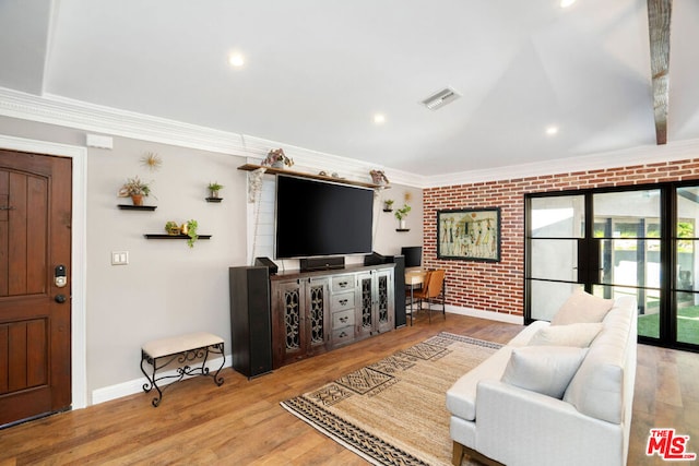 living room with wood-type flooring, ornamental molding, and brick wall