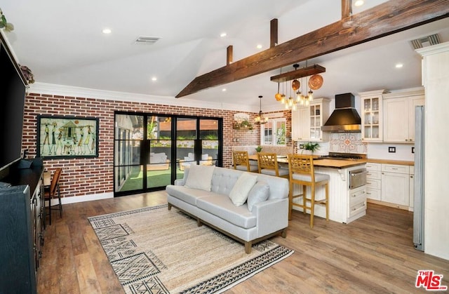 living room featuring a notable chandelier, wood-type flooring, lofted ceiling with beams, and brick wall