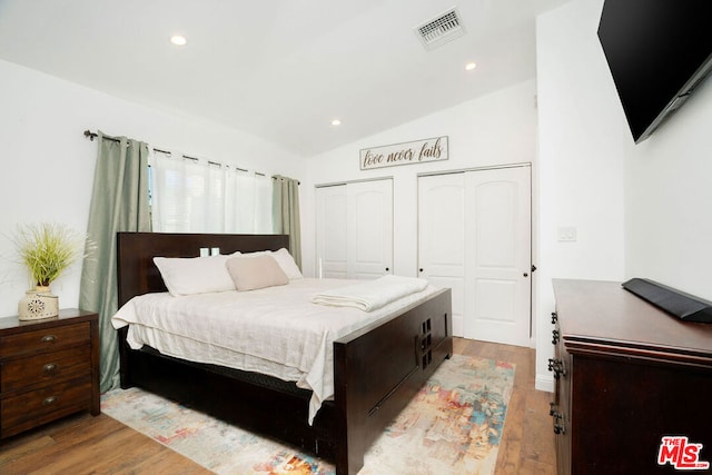 bedroom with vaulted ceiling, light hardwood / wood-style flooring, and two closets