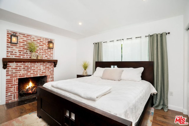 bedroom with hardwood / wood-style floors and a brick fireplace