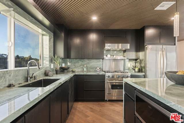 kitchen with sink, light stone counters, appliances with stainless steel finishes, pendant lighting, and exhaust hood