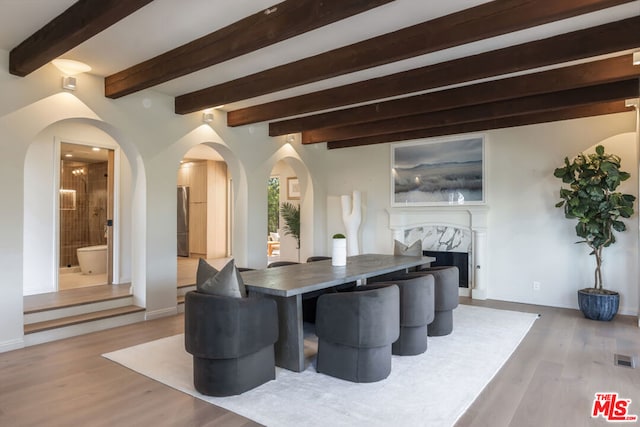 dining area with a premium fireplace, beam ceiling, and light hardwood / wood-style flooring