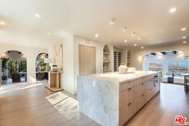 kitchen featuring light brown cabinets, oven, a spacious island, and light wood-type flooring