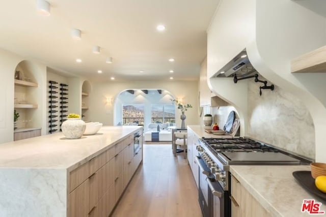 kitchen featuring light brown cabinetry, light hardwood / wood-style flooring, stainless steel range, built in features, and a large island