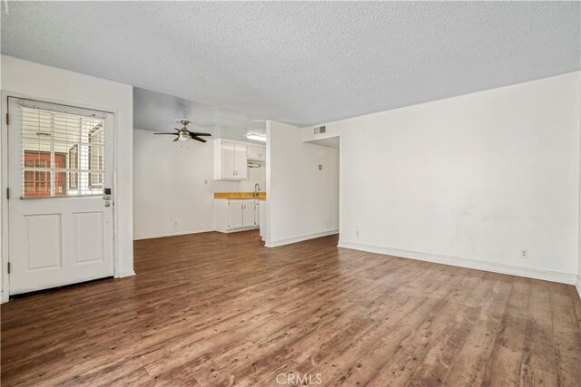 unfurnished living room with hardwood / wood-style flooring, ceiling fan, sink, and a textured ceiling