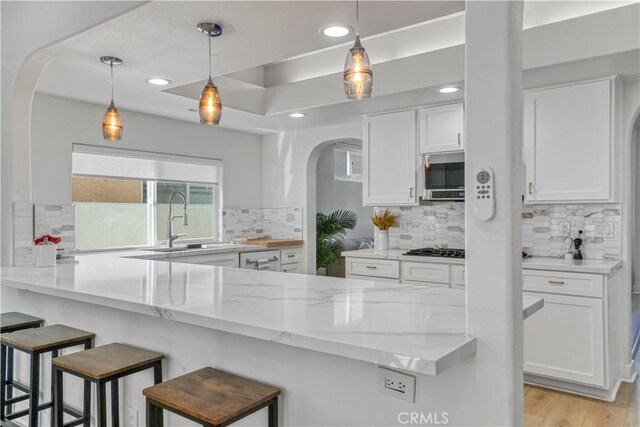 kitchen featuring a breakfast bar area, white cabinets, light stone counters, and kitchen peninsula