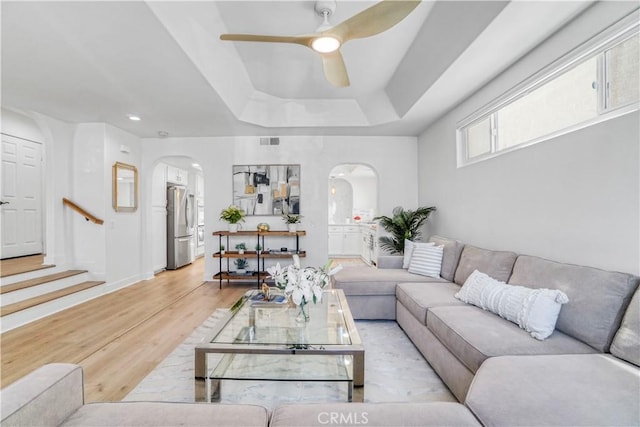 living room featuring ceiling fan, light hardwood / wood-style floors, and a tray ceiling