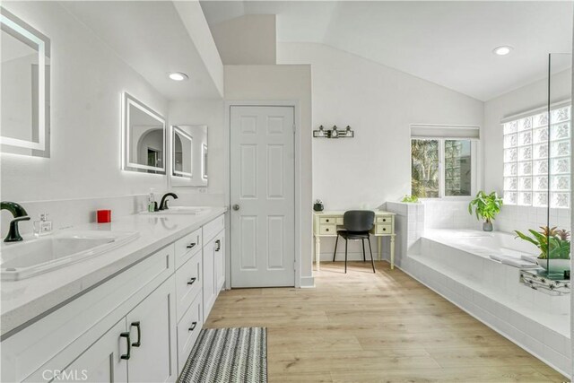 bathroom with wood-type flooring, vaulted ceiling, vanity, and tiled tub