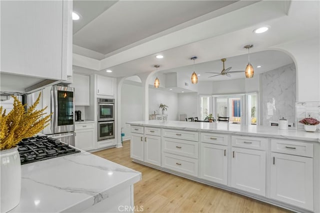 kitchen featuring pendant lighting, white cabinetry, stainless steel appliances, light stone counters, and light hardwood / wood-style floors