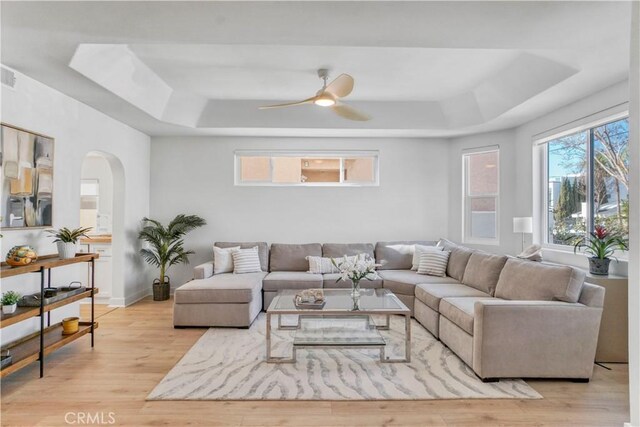 living room with ceiling fan, a tray ceiling, and light hardwood / wood-style flooring