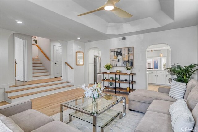 living room with light hardwood / wood-style flooring, a raised ceiling, and ceiling fan