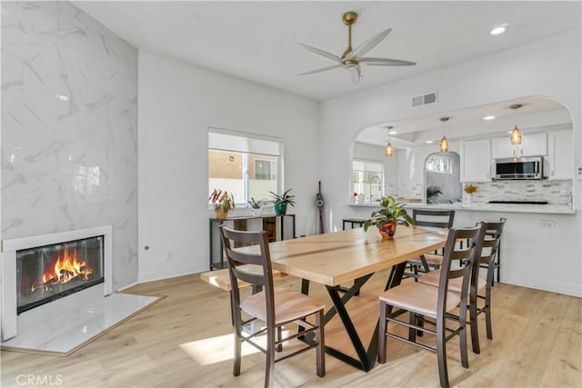 dining area featuring sink, a premium fireplace, ceiling fan, and light wood-type flooring