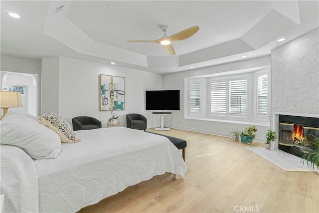 bedroom featuring ceiling fan, hardwood / wood-style floors, a fireplace, and a tray ceiling