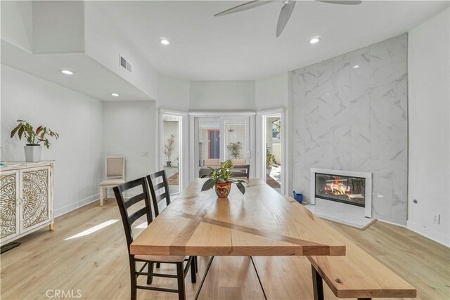 dining room with ceiling fan, light wood-type flooring, and a high end fireplace