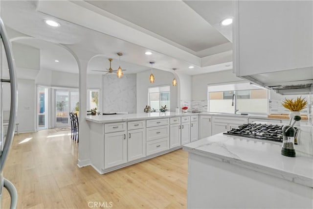 kitchen featuring sink, white cabinetry, hanging light fixtures, light wood-type flooring, and light stone countertops