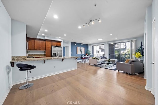 kitchen featuring light hardwood / wood-style flooring, stainless steel refrigerator with ice dispenser, light stone countertops, a kitchen bar, and kitchen peninsula