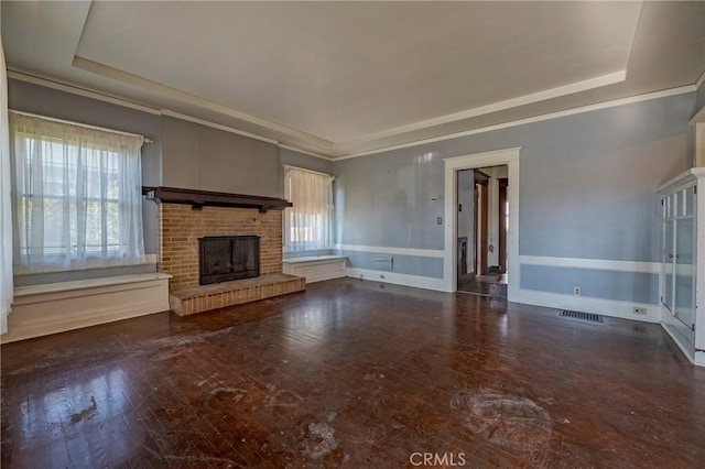 unfurnished living room featuring ornamental molding, a tray ceiling, and a brick fireplace