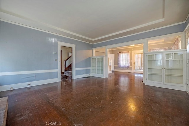 unfurnished living room featuring a raised ceiling, crown molding, and dark wood-type flooring