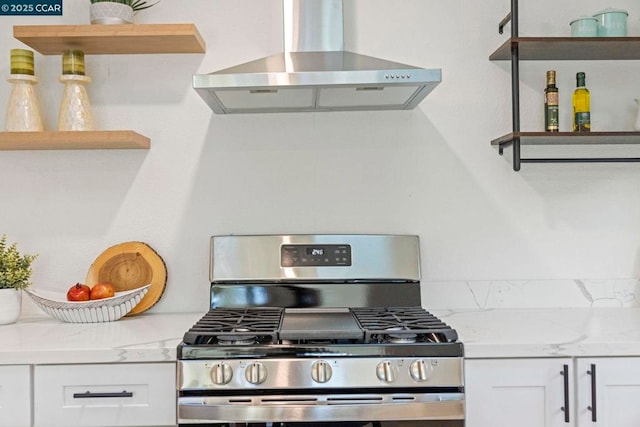 kitchen featuring light stone counters, wall chimney exhaust hood, stainless steel gas range, and white cabinets