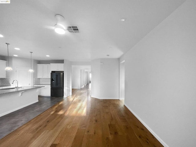 kitchen featuring black fridge with ice dispenser, hanging light fixtures, dark hardwood / wood-style floors, white cabinets, and backsplash