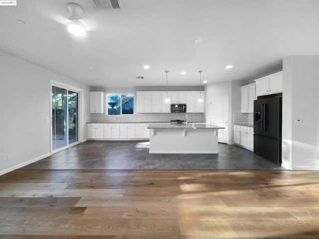 kitchen with a breakfast bar area, a kitchen island with sink, hanging light fixtures, white cabinets, and black refrigerator with ice dispenser