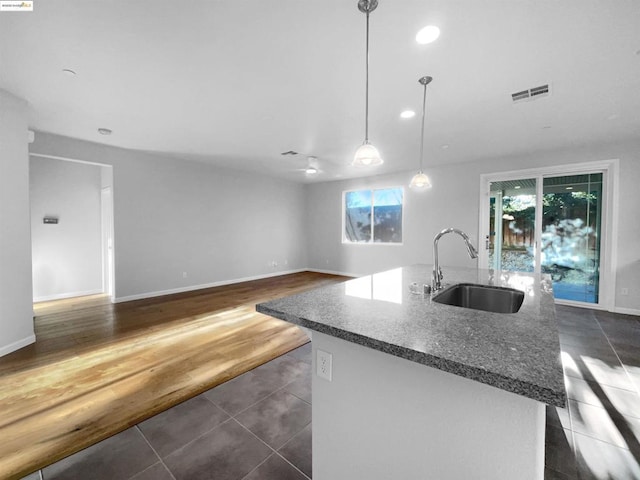 kitchen with sink, decorative light fixtures, a center island with sink, dark tile patterned floors, and dark stone counters