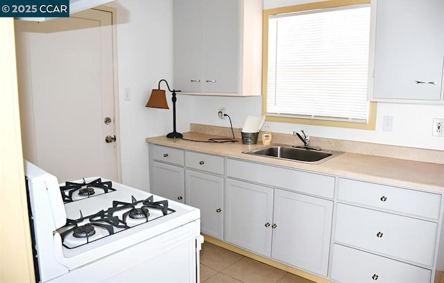 kitchen with white cabinetry, sink, light tile patterned flooring, and white gas range