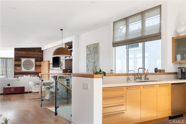 kitchen featuring pendant lighting, light countertops, stainless steel dishwasher, wood finished floors, and a sink