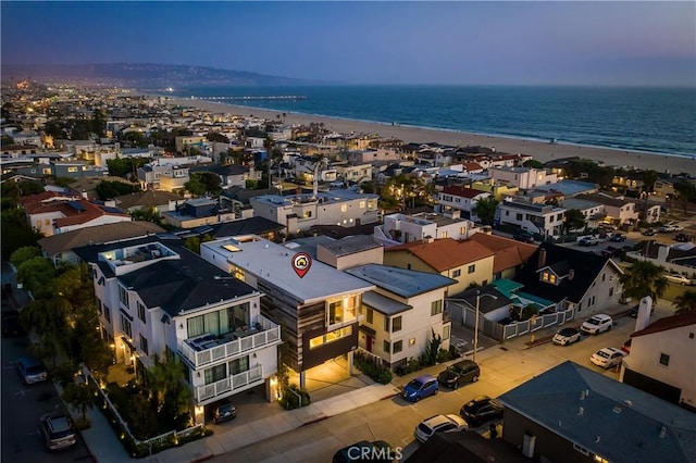 aerial view at dusk featuring a water view and a beach view