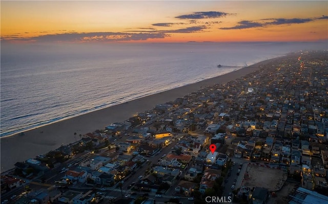 aerial view at dusk featuring a view of the beach and a water view