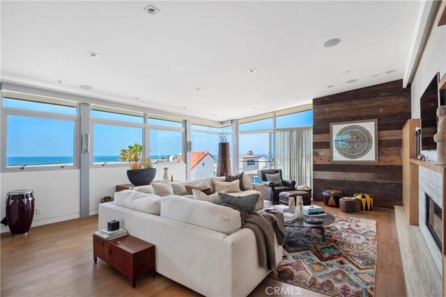 living room with a fireplace, light hardwood / wood-style floors, wooden walls, and a water view