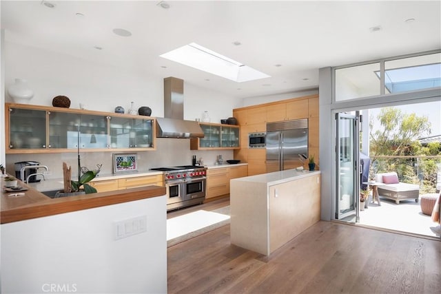 kitchen with light brown cabinetry, wood-type flooring, backsplash, exhaust hood, and built in appliances