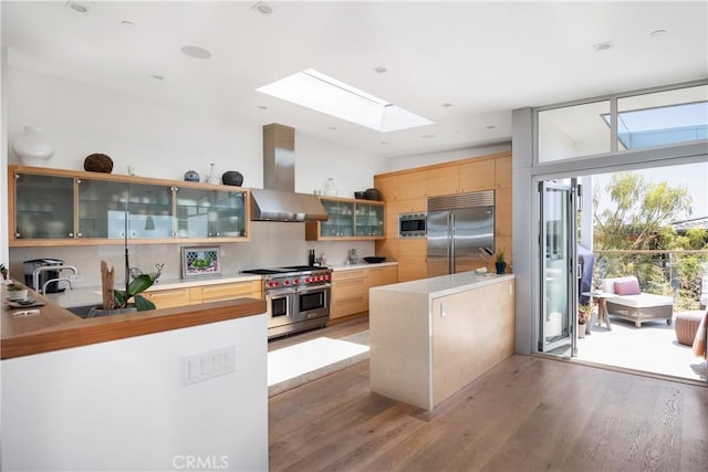 kitchen with tasteful backsplash, range hood, light wood-style floors, a peninsula, and built in appliances