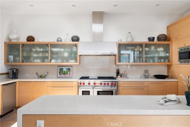 kitchen featuring glass insert cabinets, light countertops, decorative backsplash, stainless steel appliances, and wall chimney exhaust hood