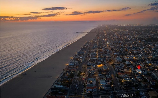 aerial view at dusk featuring a water view and a beach view