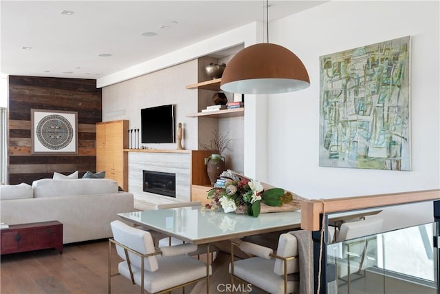 dining space with dark wood-type flooring, a premium fireplace, and wooden walls