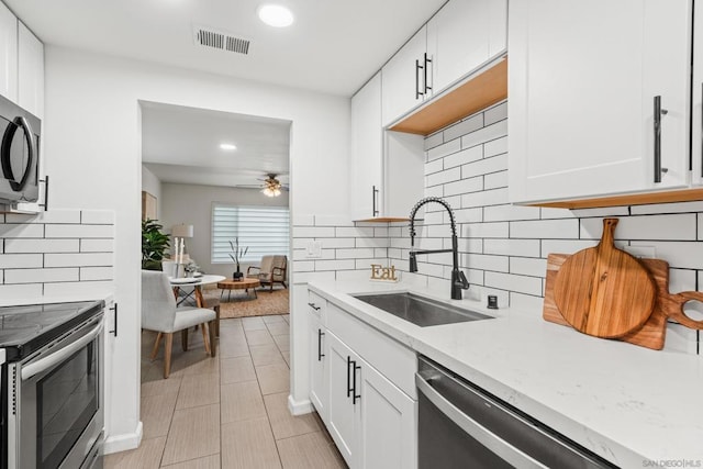 kitchen featuring appliances with stainless steel finishes, sink, white cabinets, decorative backsplash, and light stone counters