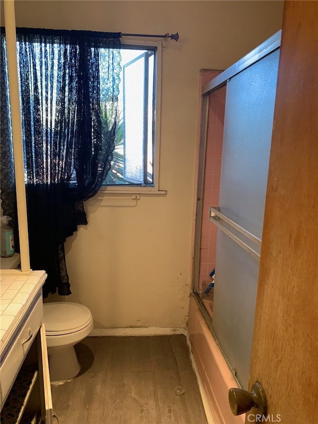 full bathroom featuring hardwood / wood-style flooring, vanity, enclosed tub / shower combo, and toilet