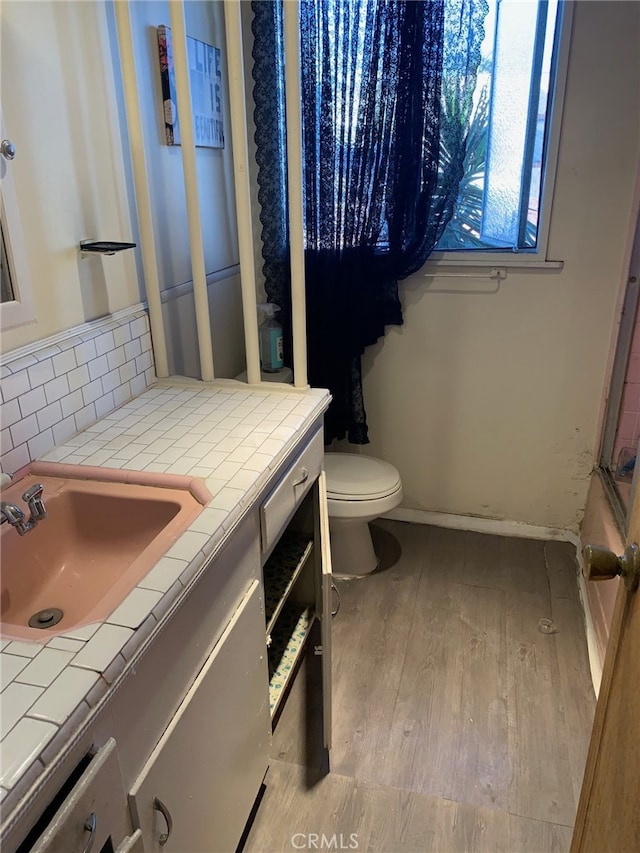 bathroom featuring hardwood / wood-style floors, tasteful backsplash, a shower, vanity, and toilet