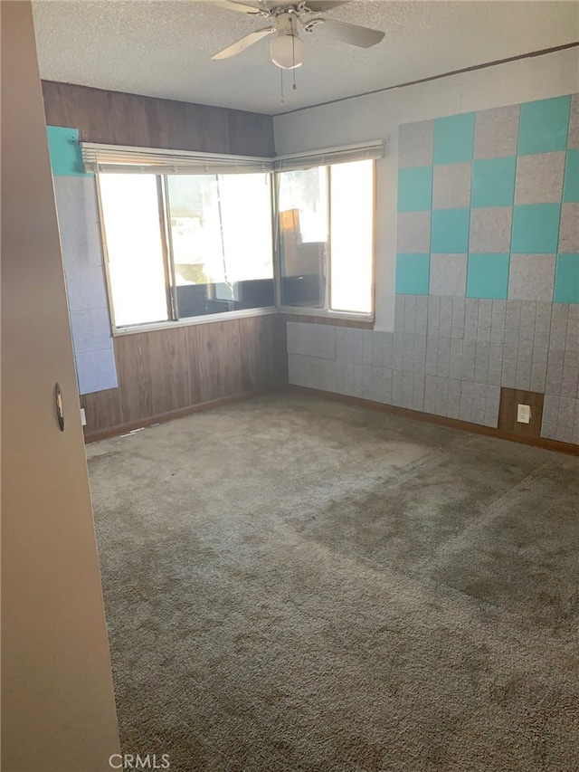 unfurnished room featuring ceiling fan, carpet, a textured ceiling, and wood walls