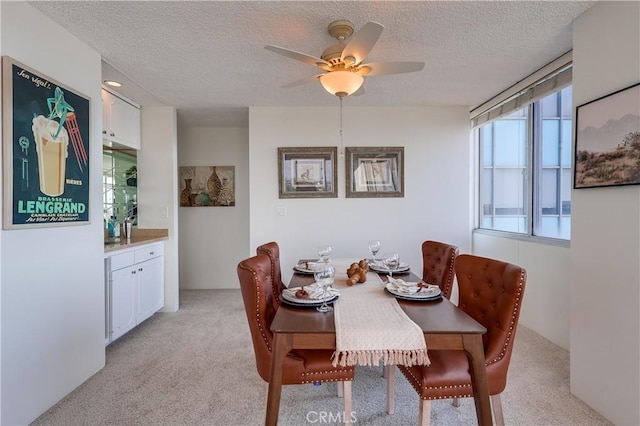 dining room featuring light colored carpet, ceiling fan, and a textured ceiling