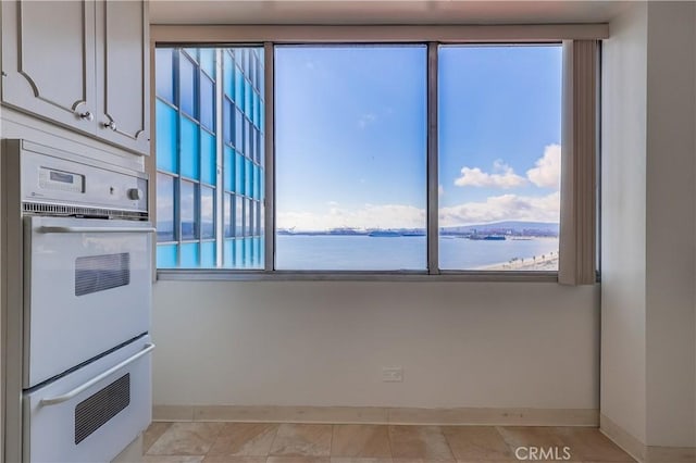 kitchen with a water view, double oven, white cabinets, light tile patterned floors, and baseboards