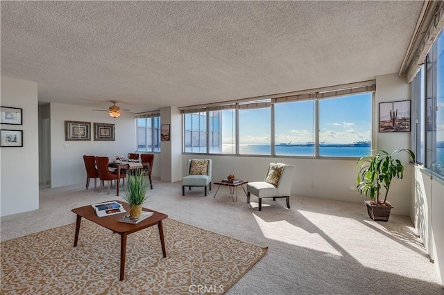 carpeted living area with a water view and a textured ceiling