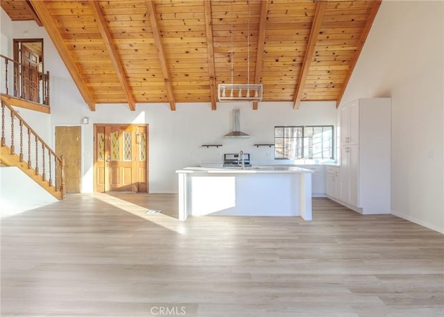 kitchen featuring wall chimney range hood, wood ceiling, an island with sink, white cabinets, and light wood-type flooring