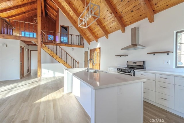 kitchen featuring white cabinetry, an island with sink, sink, stainless steel range, and wall chimney exhaust hood