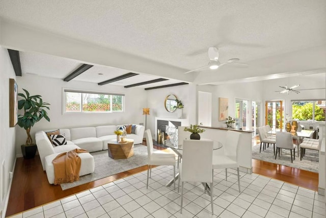 tiled living room with ceiling fan, beam ceiling, and a textured ceiling